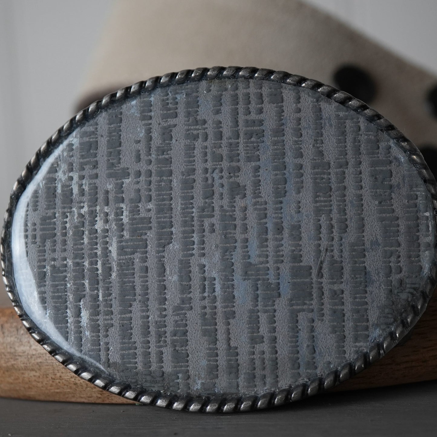 Textured belt buckle on a wooden surface with a blurred background