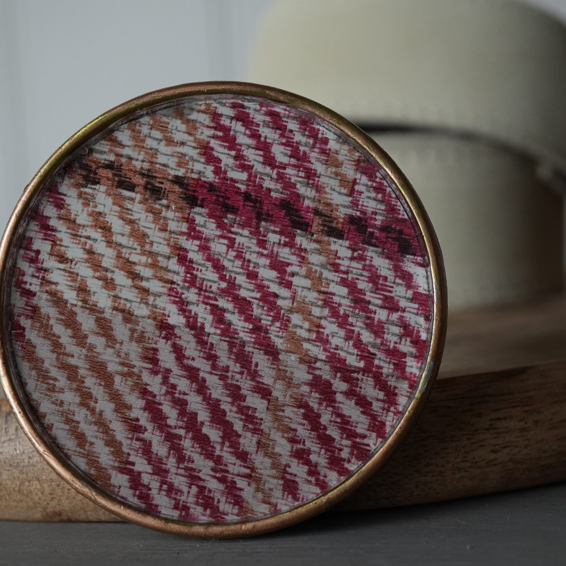 Round woven fabric sample in a gold frame on a wooden surface