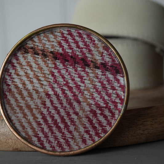 Round woven fabric sample in a gold frame on a wooden surface